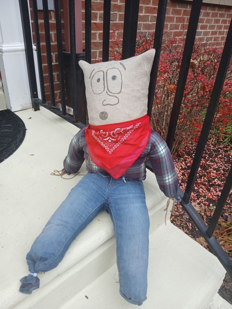 Cute little guy made out of stuffed shirt and jeans, with a red scarf.