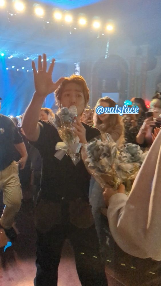 lee jinki (onew) walks up the aisle of a concert venue with a microphone and bouquet of flowers