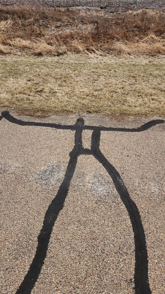 Tar filled crack in asphalt walking path that looks like a person 