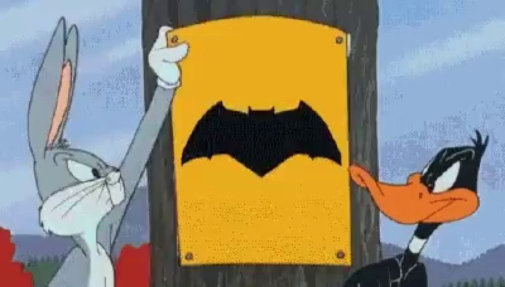 bugs bunny and daffy duck are standing next to each other holding a sign that says batman on it .