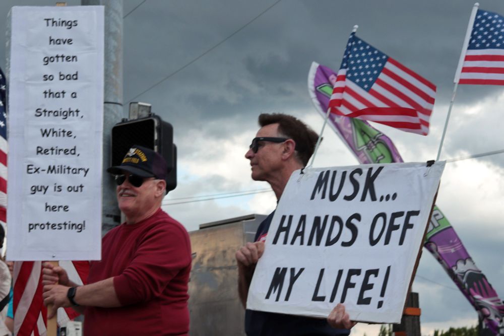 Two protestors stand holding signs, one of whom is wearing a veteran’s baseball cap. The protestor on the right holds a sign that reads: “MUSK… HANDS OFF MY LIFE!”. Two small US flags fly from the top of the sign. The protestor on the right carries a sign which reads "Things have gotten so bad that a Straight, White, Retired, Ex-Military guy is out here protesting!"

At 5:00pm on May 7th, 2025, protestors gathered at the intersection of NE Fourth Plain Blvd and NE Andresen Rd outside the Vancouver, WA, Tesla dealership to protest the fascist regime of President Donald Trump and unelected billionaire Elon Musk.
