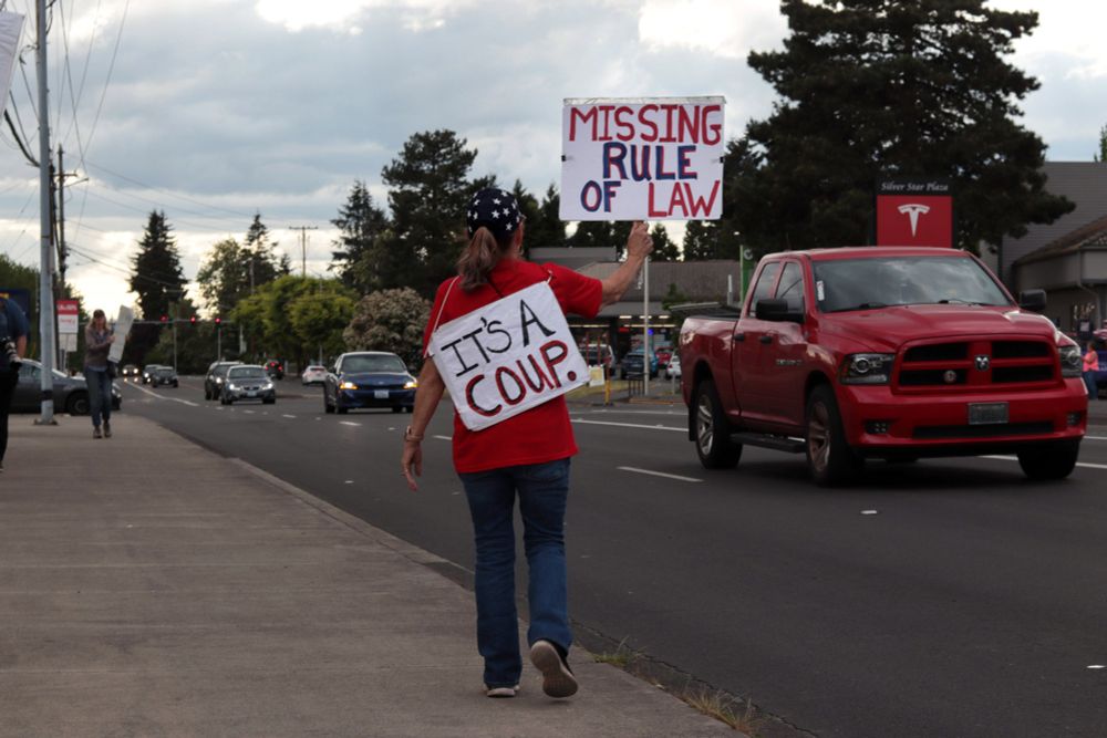 A protestor walks away from the viewer along the sidewalk. The protestor holds a sign that reads: “MISSING RULE OF LAW”. Another picket sign that is attached to the protestor’s back reads: “IT’S A COUP.” In the background, a red truck passes and the sign for the Tesla dealership is visible.

At 5:00pm on May 7th, 2025, protestors gathered at the intersection of NE Fourth Plain Blvd and NE Andresen Rd outside the Vancouver, WA, Tesla dealership to protest the fascist regime of President Donald Trump and unelected billionaire Elon Musk.
