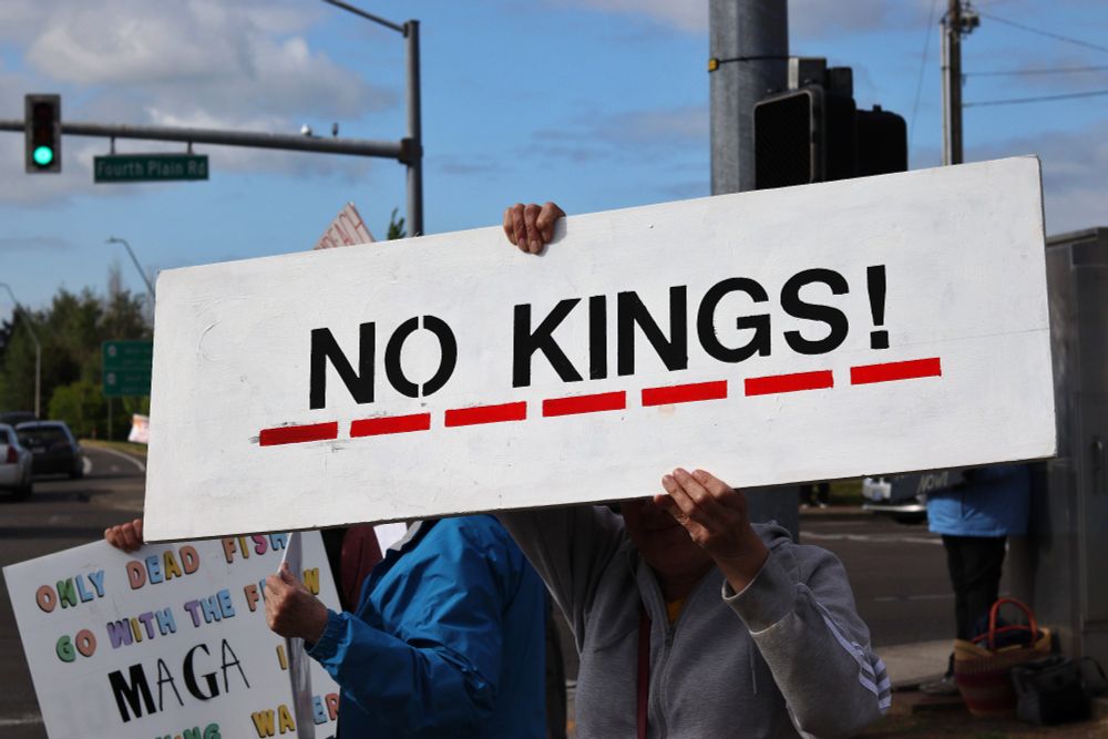 A protestor holds a large picket sign that covers their face and the faces of surrounding protestors. The sign reads: “NO KINGS!”. The words on the sign are underlined by red dashes. 

At 5:00pm on May 14th, 2025, protestors gathered outside the Vancouver, WA Tesla dealership to protest the fascist regime of US President Donald Trump and unelected billionaire oligarch Elon Musk. 

