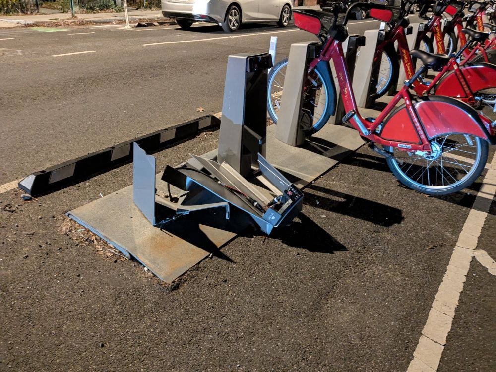 Capital Bikeshare station in the street. One of the upright bike docks is mangled and in pieces 