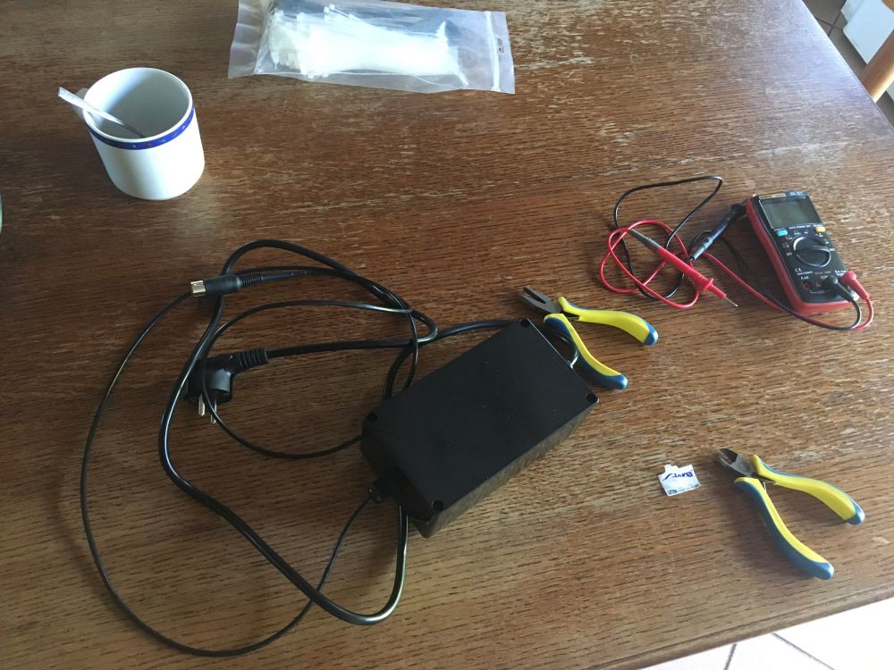 The aftermath of assembling the power supply. Shows the PSU, pliers and multimeter on a table