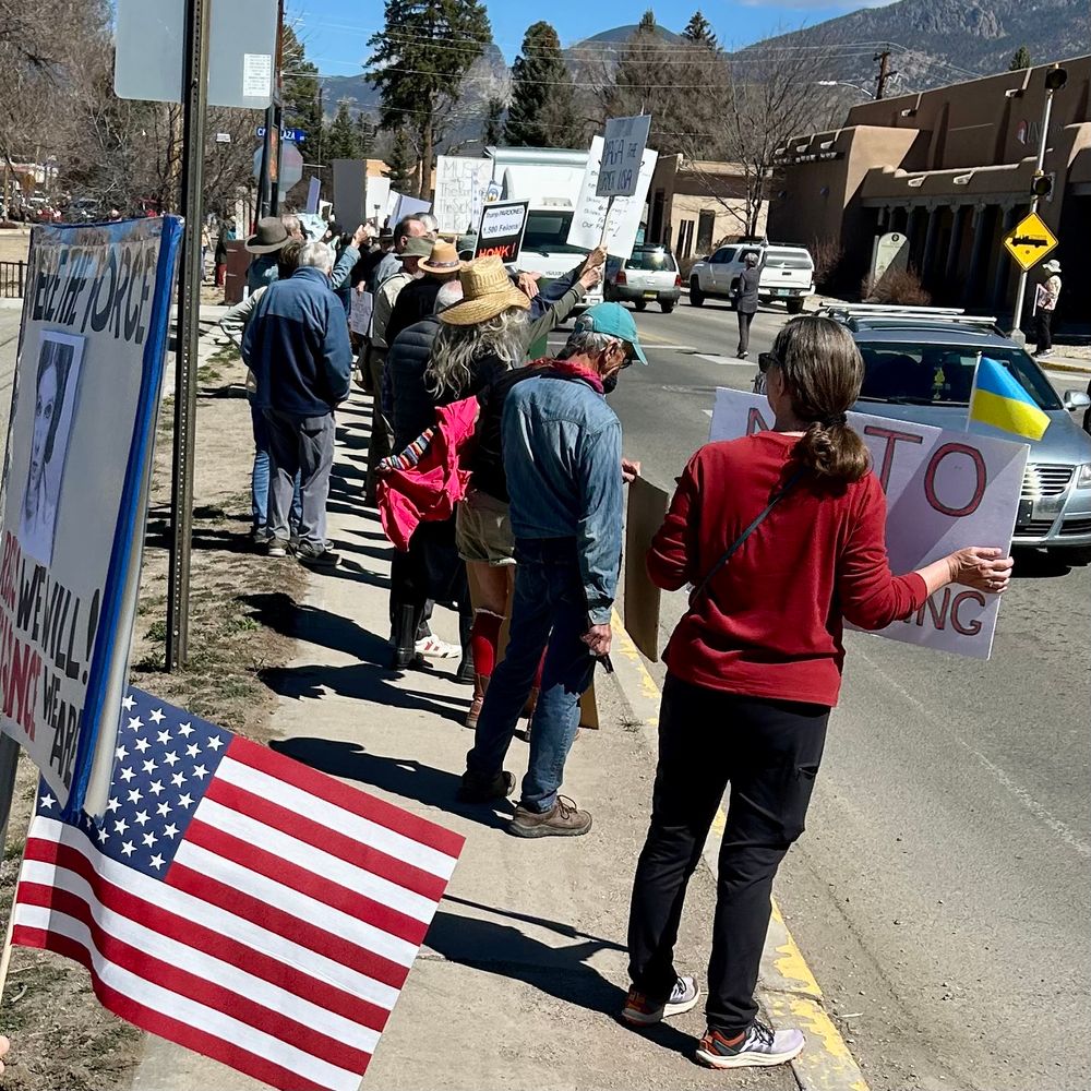 Hundreds of protesters holding signs and American flags standing next to street in Taos, New Mexico