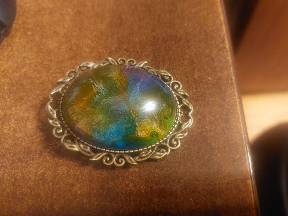 A large oval resin pendant with blue, green and yellow swirling colouring. It looks a little like moss or mold is growing inside it.