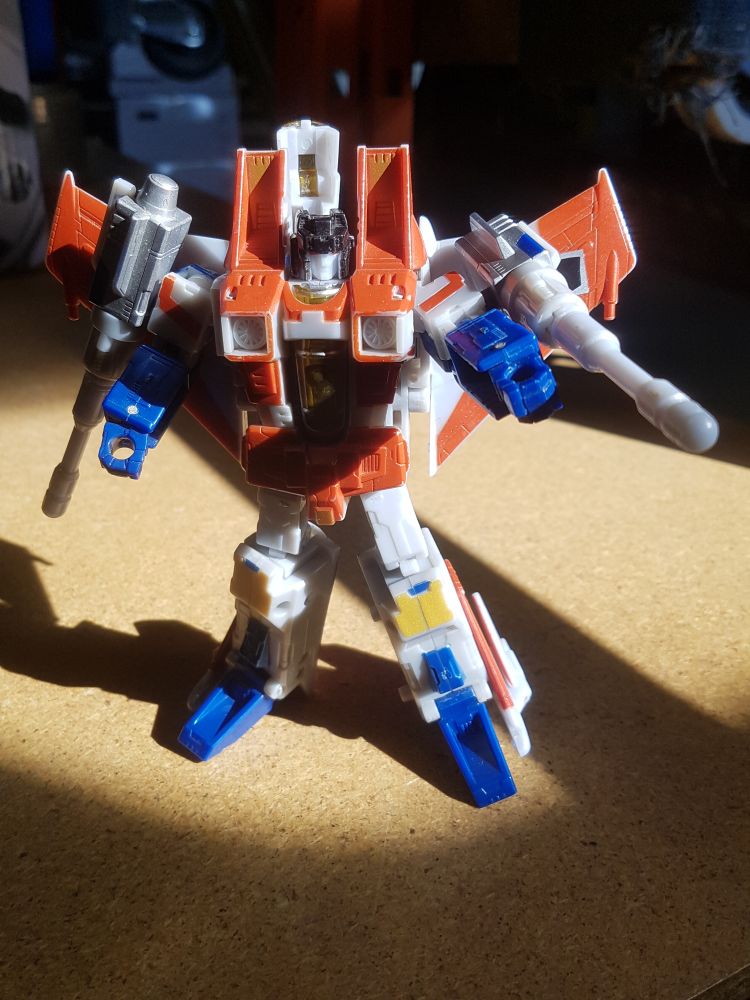 Starscream posed pointing his weapon on a workbench in the sunlight.