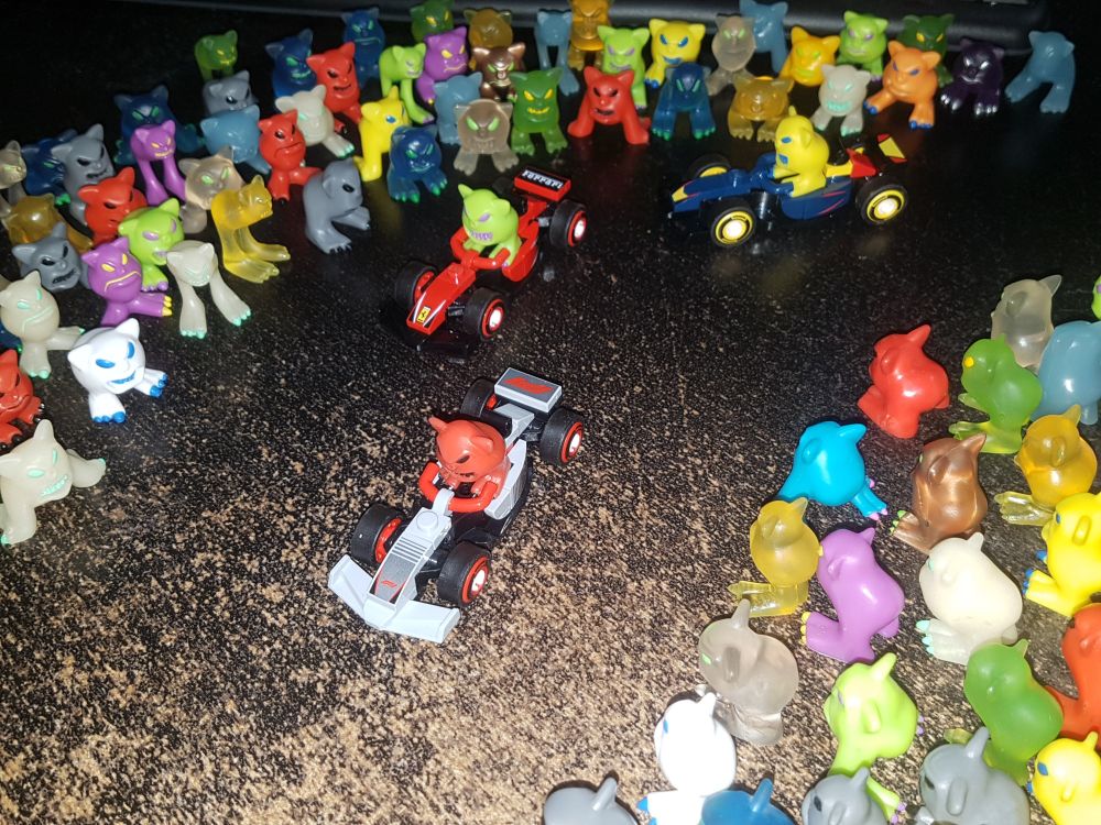 A picture of a lot of Mordles, with three of them sitting in small LEGO race cars.