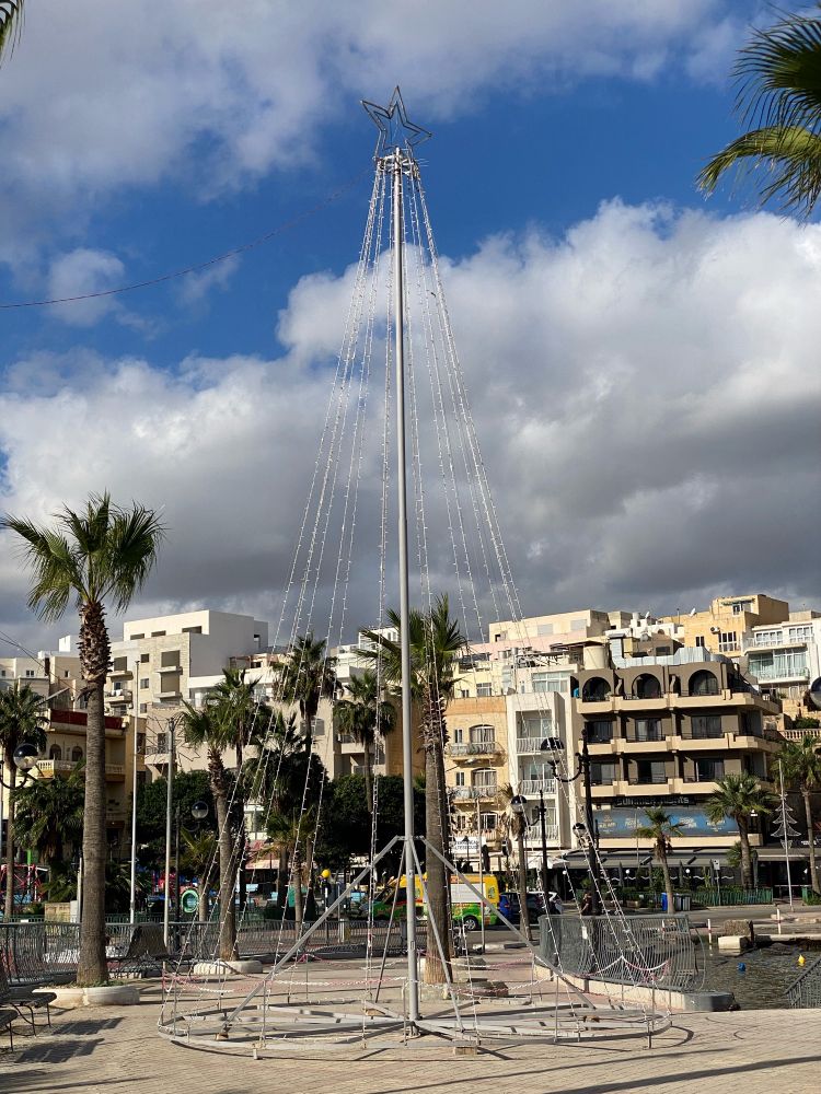 Das Metallgerüst mit Lichterkette neben Palmen und der Marina