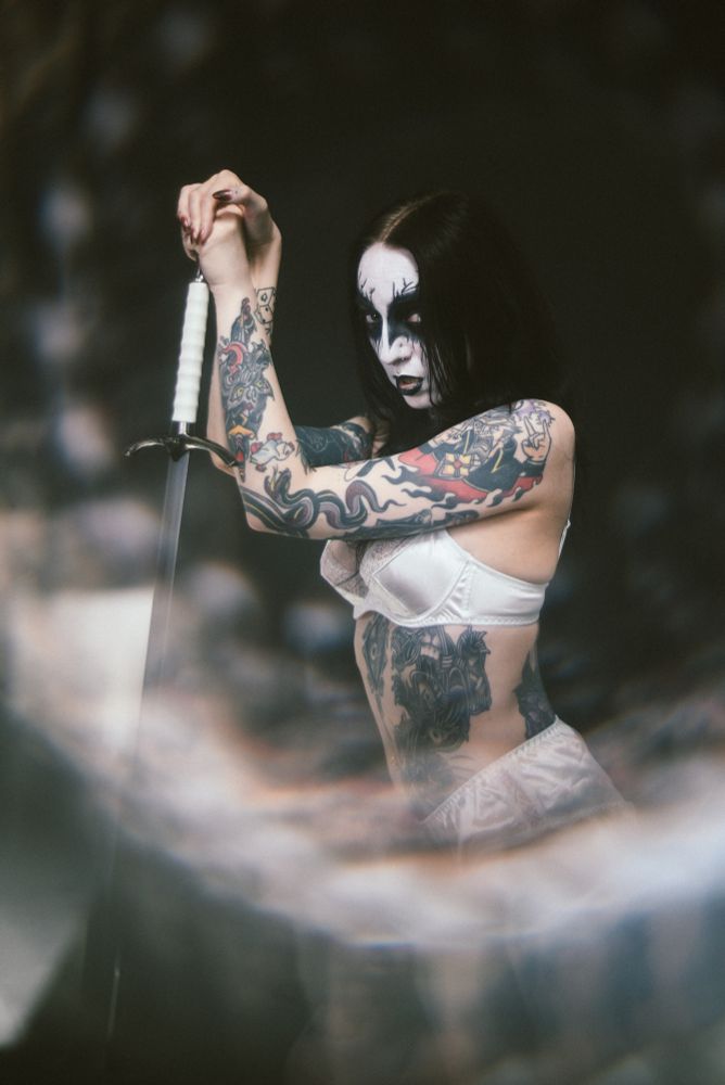 tattooed woman wearing corpse paint with white lingerie holding a sword