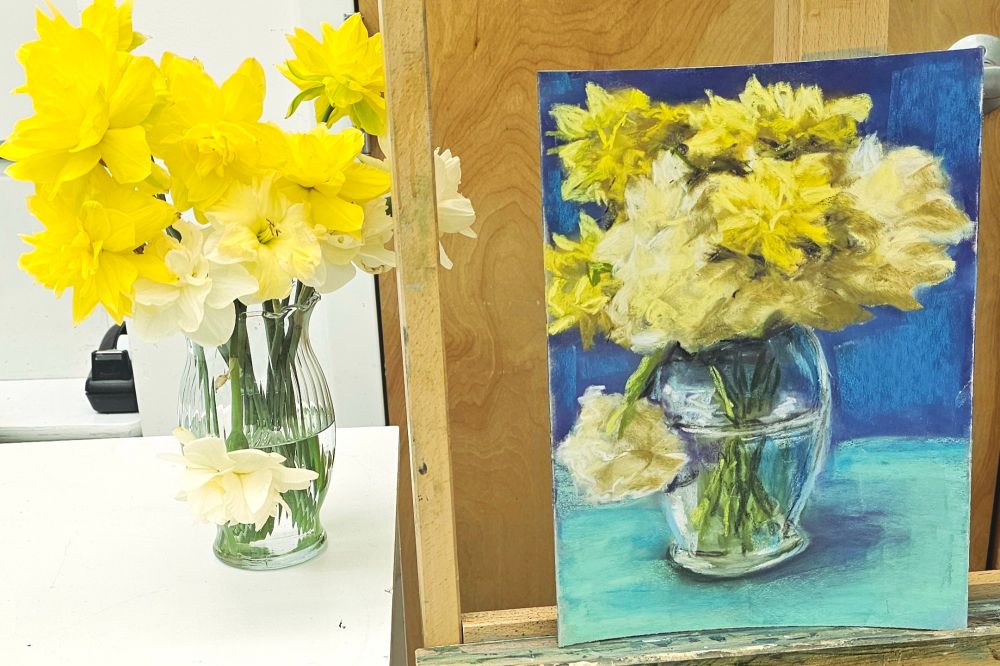 Daffodils in a vase, next to soft pastel painting of same. 