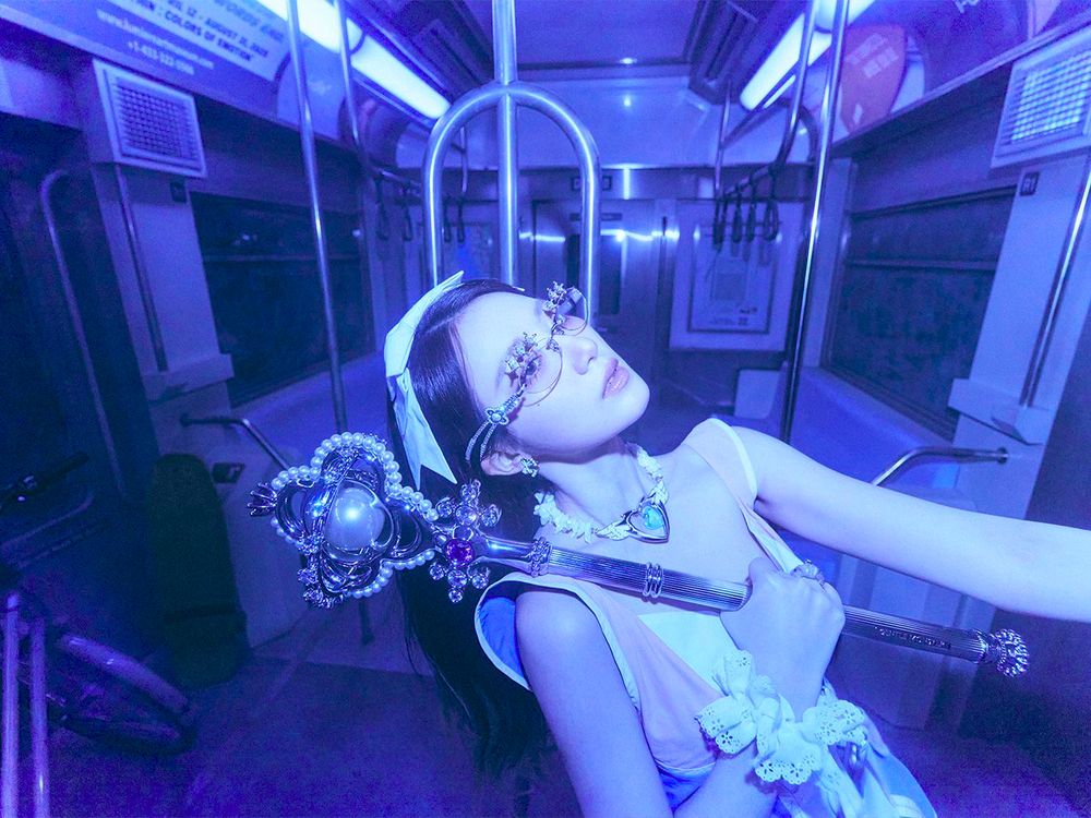Shuhua posing in a blue-lit subway car, holding a jeweled magic staff close to her face