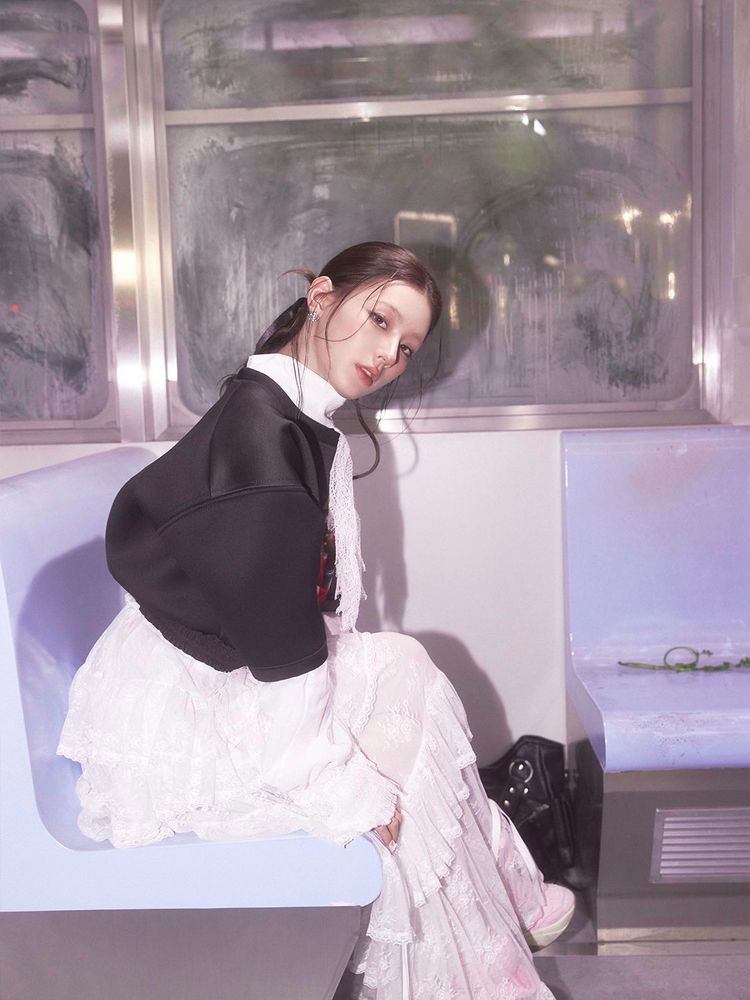 Miyeon, wearing a white lace dress and a black jacket, sits on a subway seat, looking towards the camera