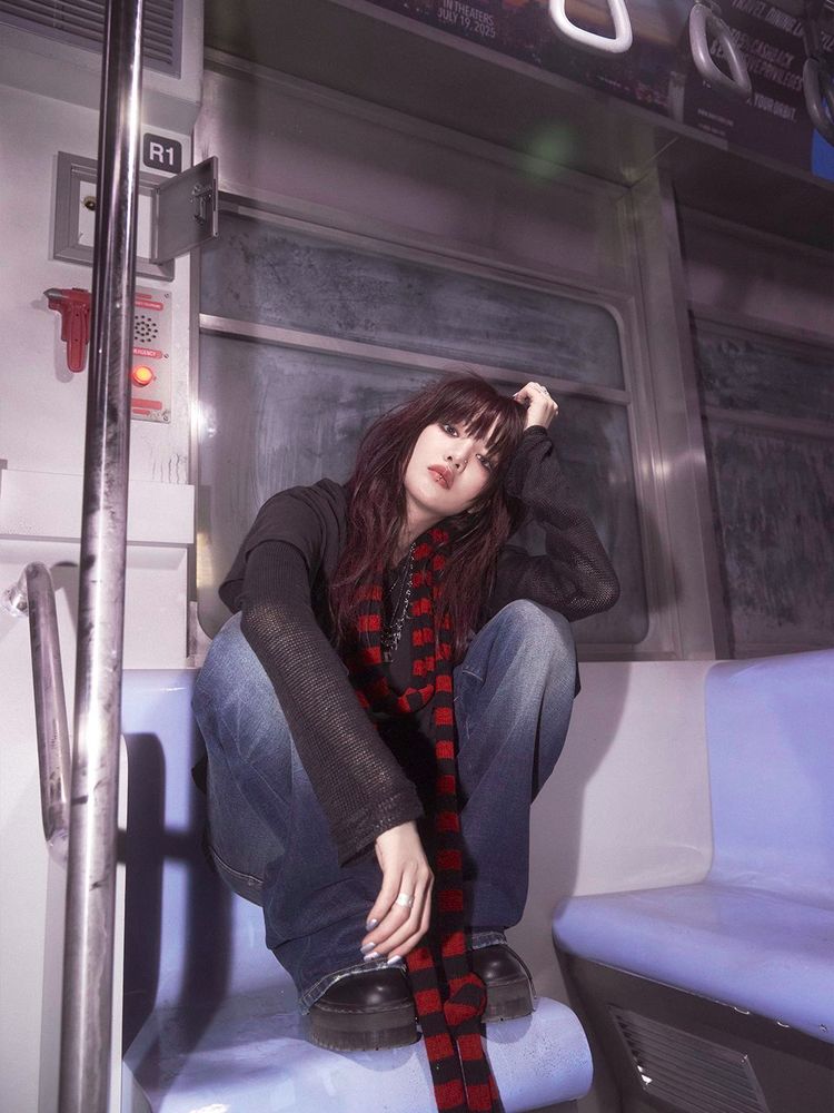 Minnie is sitting on her feet on a bench in a subway car. She is wearing an urban outfit with a red and black striped scarf