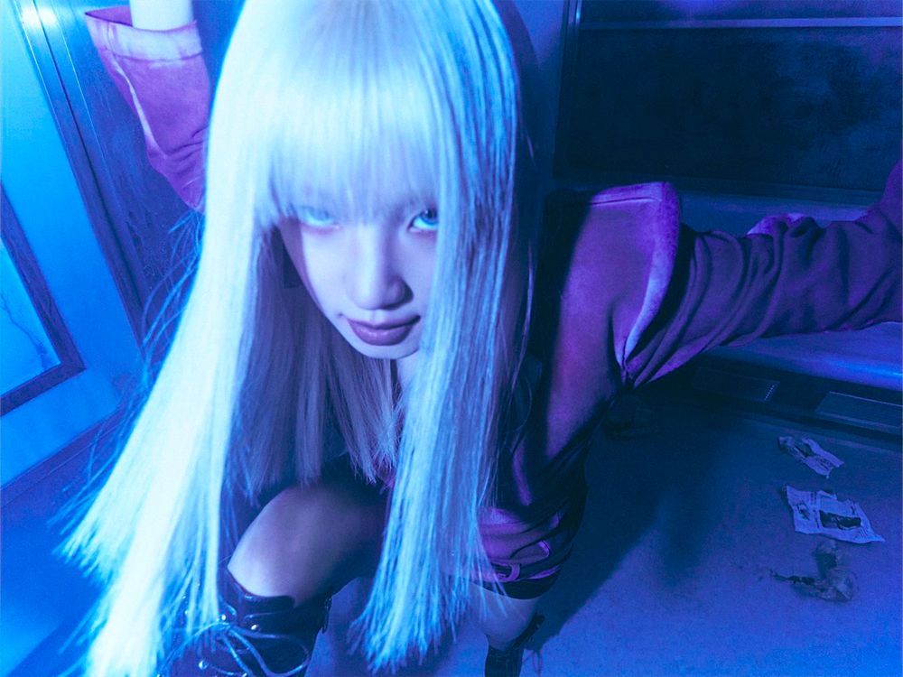 A close-up photo of Yuqi inside the blue-lit subway car, she is gazing at the camera