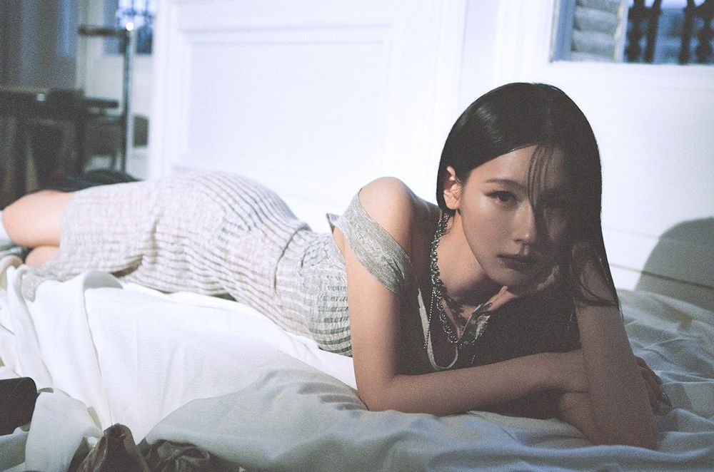 Miyeon (I-DLE) lying on a bed, head resting on her hand, gazing at the camera
