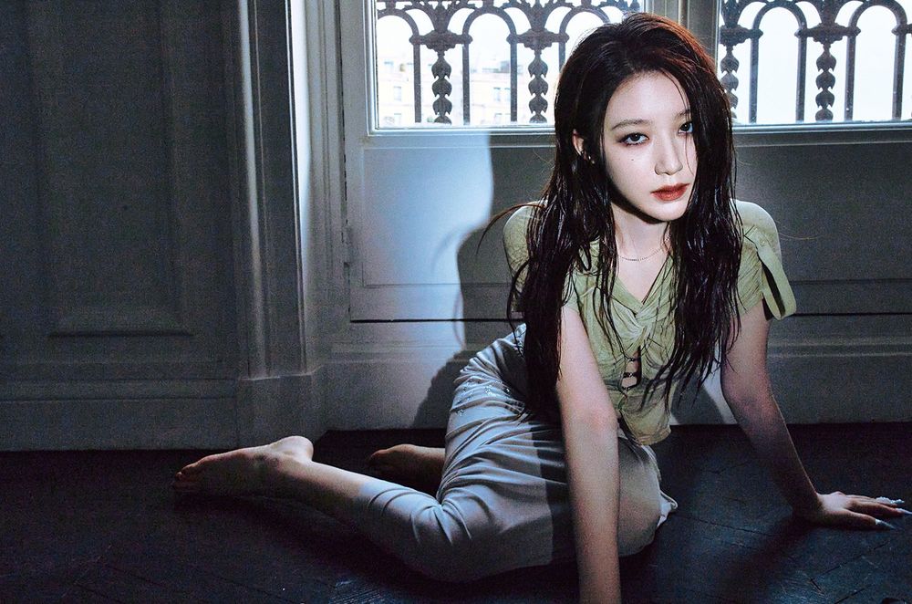 Shuhua sitting on the floor, with both hands placed on the ground, gazing into the camera