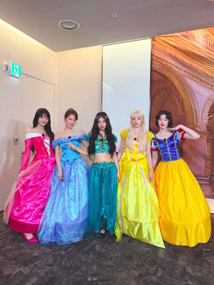 i-dle members posing together dressed as Disney princesses: Minnie as Aurora, Miyeon as Cinderella, Soyeon as Jasmine, Yuqi as Belle, and Shuhua as Snow White