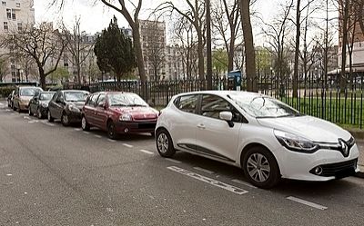 Multiple cars are parked in a street in Paris. There are no markers indicating the size of an individual parking spot.