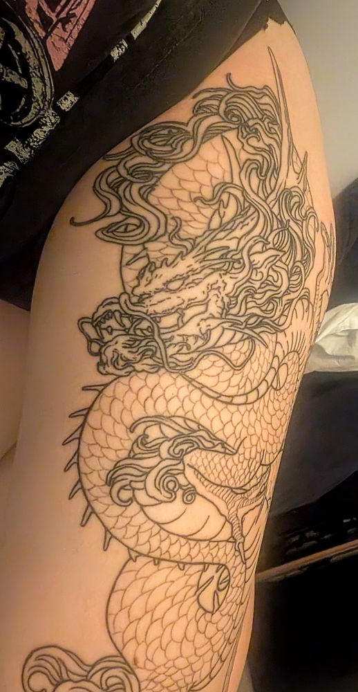 Close up photo of Karin's thigh with part of a dragon tattoo. You can see its head and the top half of it's body 