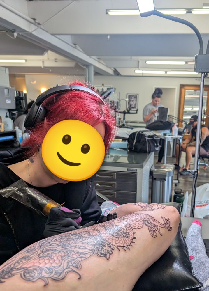 My tattoo artist actively tattooing a dragon on my mid-thigh. 