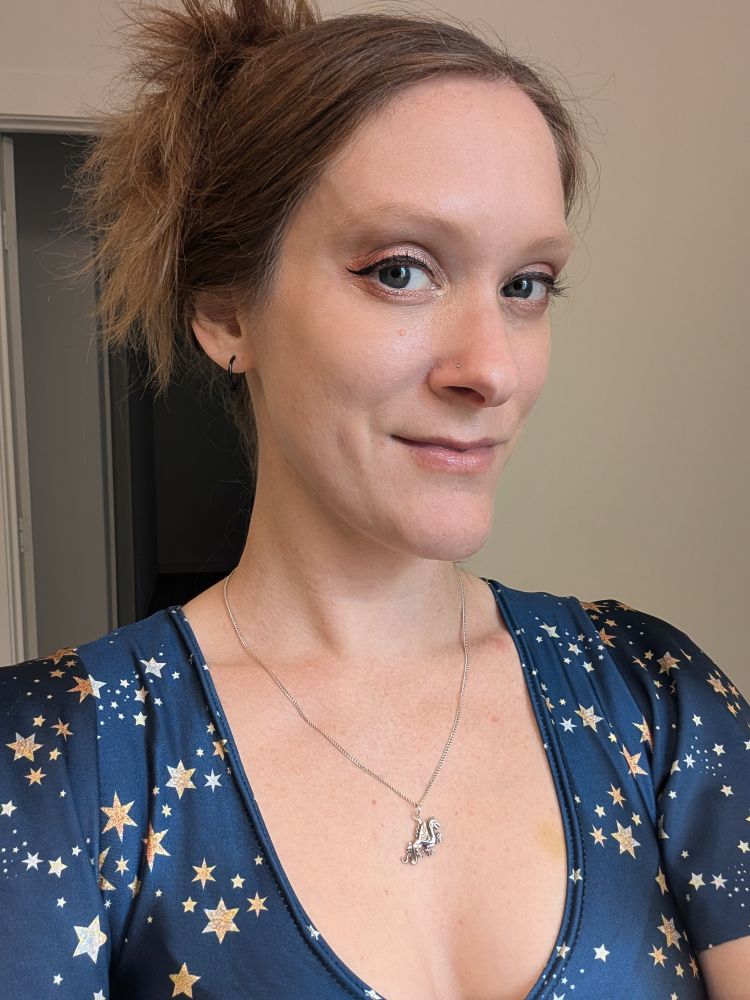 A photo of Karin from the front and from the chest up, dressed in star patterned jumpsuit and wearing some nice cat-eye eyeliner. Her hair is up, and she is close-mouth smiling because she doesn't always like they way her big smiles look in photos 