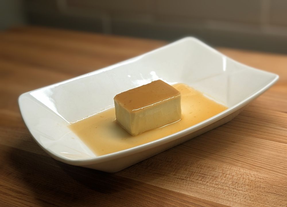 A little square of pale brown flan, covered in and resting in a lovely brown caramel sauce