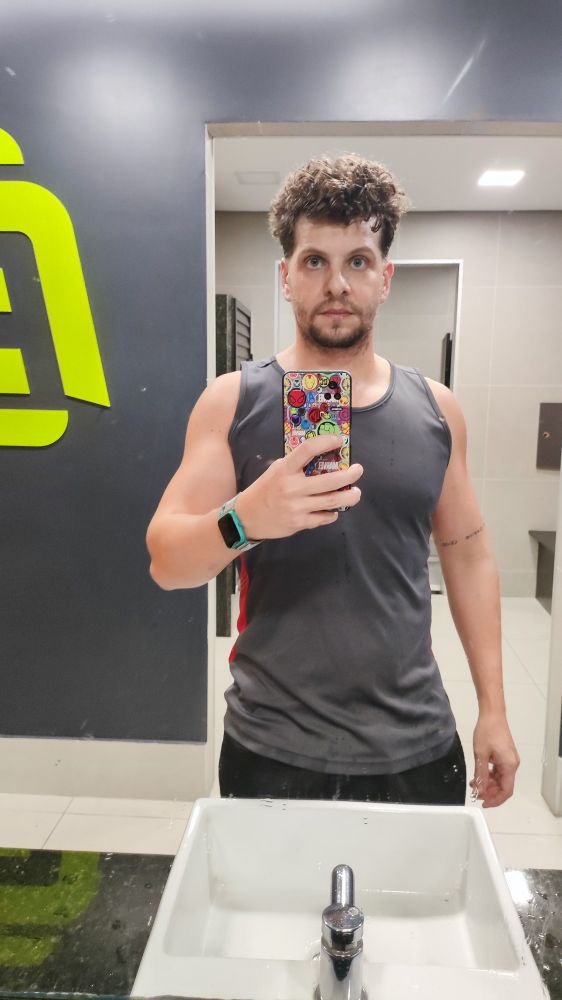 Homem de regata tirando foto no espelho do banheiro da academia 