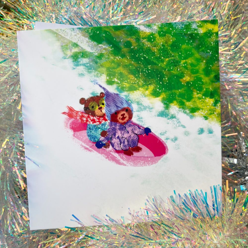 a photo of a christmas card by illustrator kip alizadeh showing two baby bears in snowsuits whizzing down a snowy hill in a sledge