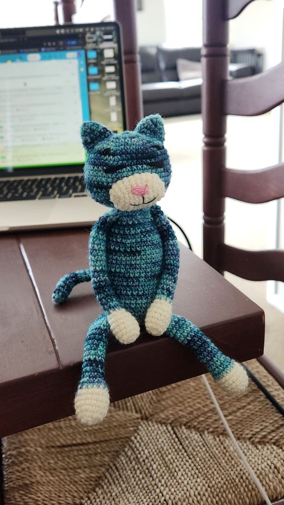 chill little blue crochet cat sitting on the edge of a table 