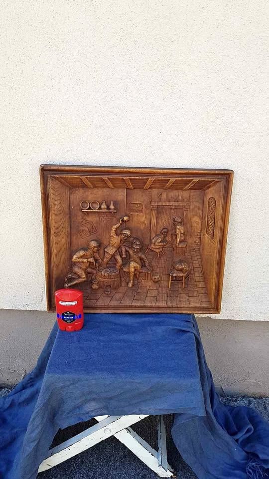 wooden "painting" of figures where one appears to be beating another about the head while a third has something that vaguely looks like a german WWII helmet on and is holding what could be knives, and is watching the others while 2 more people are in the background ignoring it all...