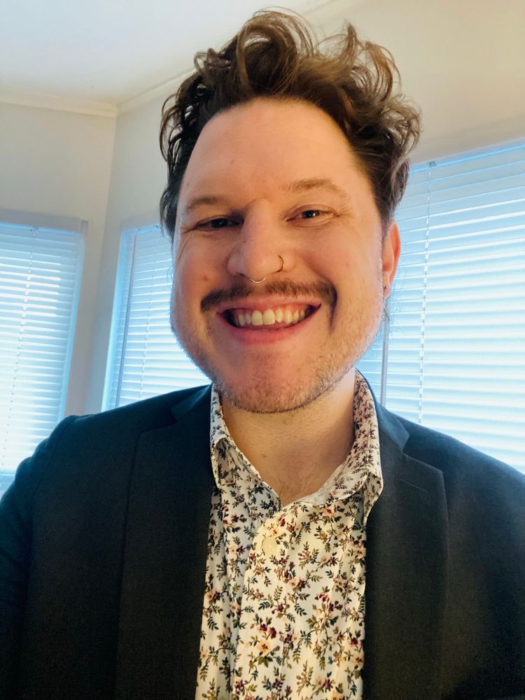 Tuck selfie in a dark gray suit and floral shirt