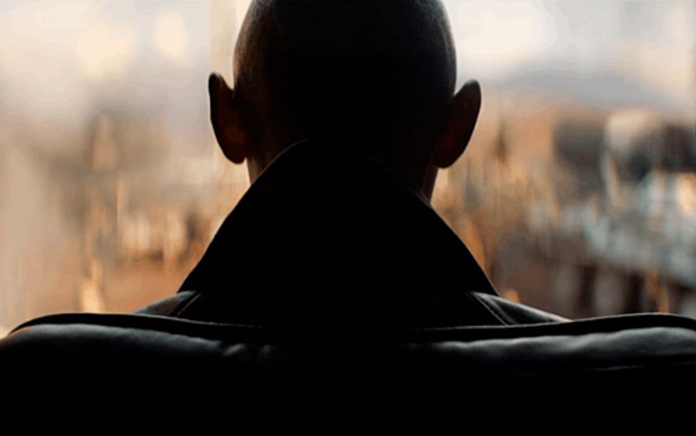 a man 's back is shown in a dark room looking out a window