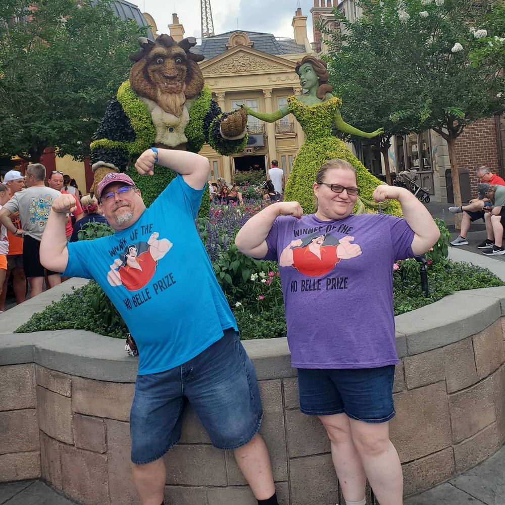 My partner and I are posing in front of the Beauty And The Beast topiary. Our T-shirts have Gaston with the caption "Winner of the No-Belle Prize."