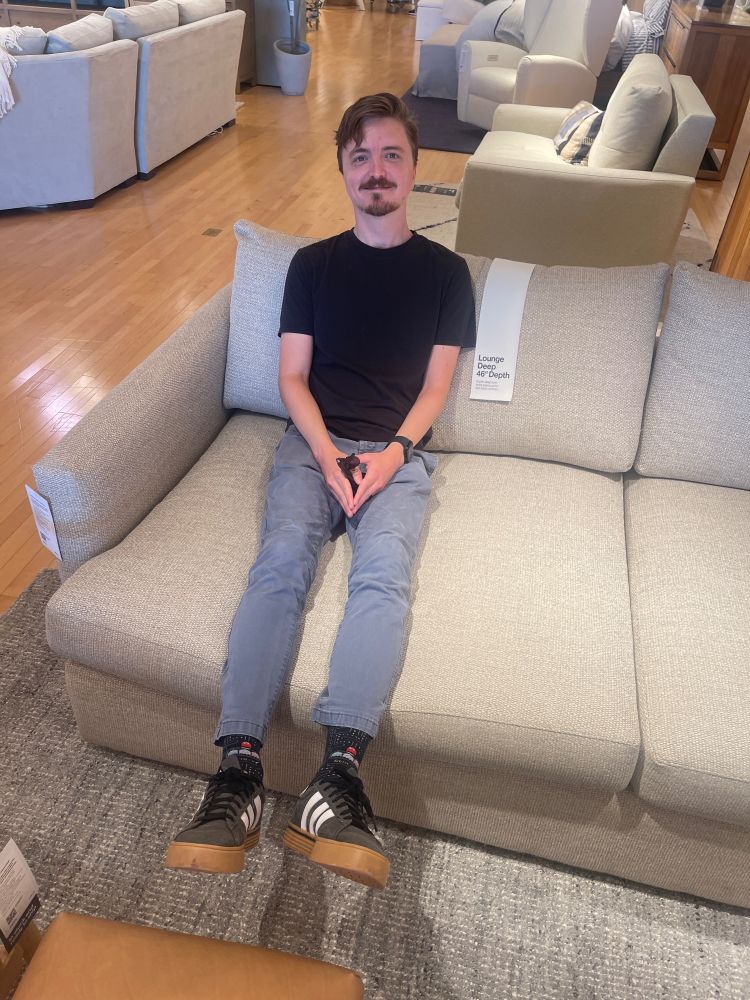 A man sits on a very deep couch, and the perspective of the couch makes him look comically small.  Also you can kind of see that he's wearing PAC-MAN socks