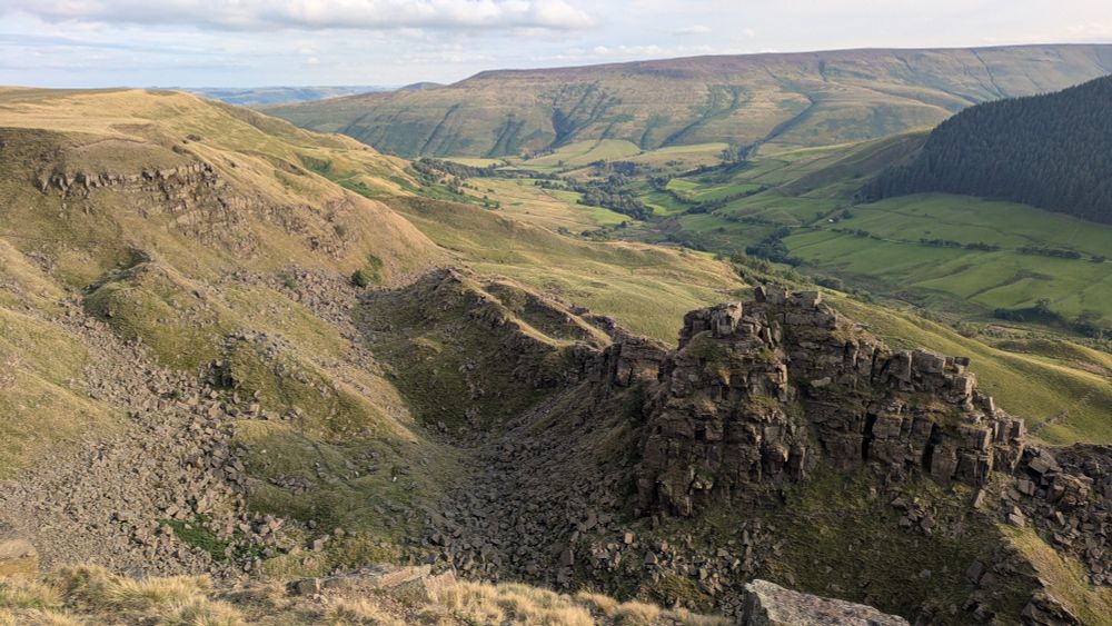 View over a cliff edge to rocky ground and a grassy valley beyond. 