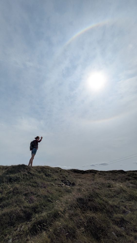 Silhouette of a person on a hill below a sun halo.