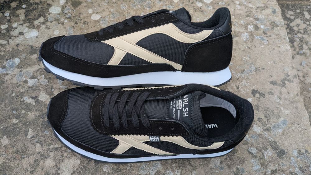 Black and white training shoes by Norman Walsh on a stone background.