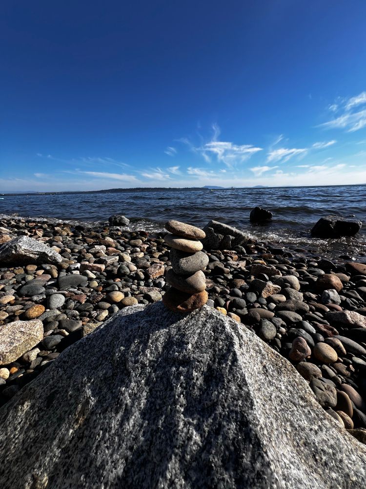 5 flat rocks stacked in front of waves and beach