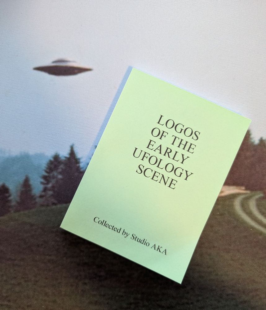 Small green book with the title "LOGOS OF THE EARLY UFOLOGY SCENE" At the bottom it says "Collected by Studio AKA"

It is on top of a deskmat that has a print of a photograph of a UFO from Billy Meier, the same one seen in the X-files "I want to believe" poster