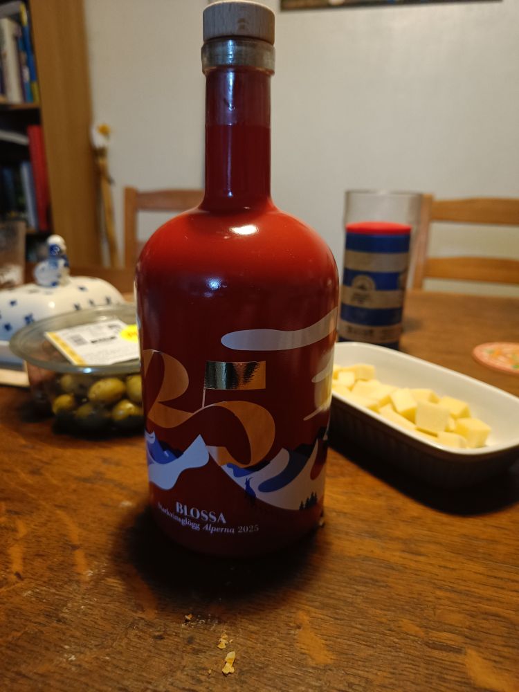 A red bottle of Blossa glögg on a wooden table with cheese and olives either side