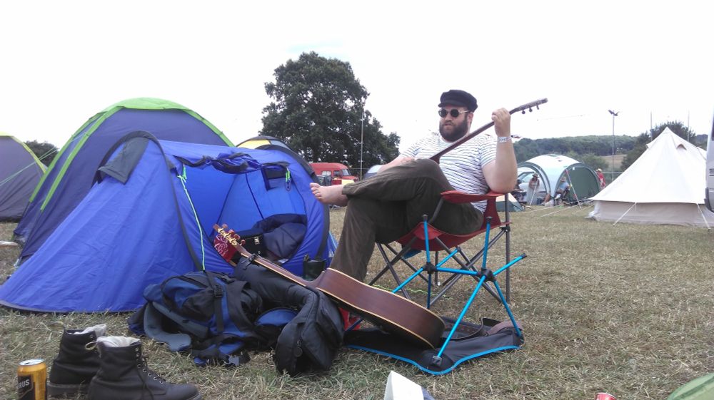 Jon looking cool af chilling outside his tent strumming his banjo 