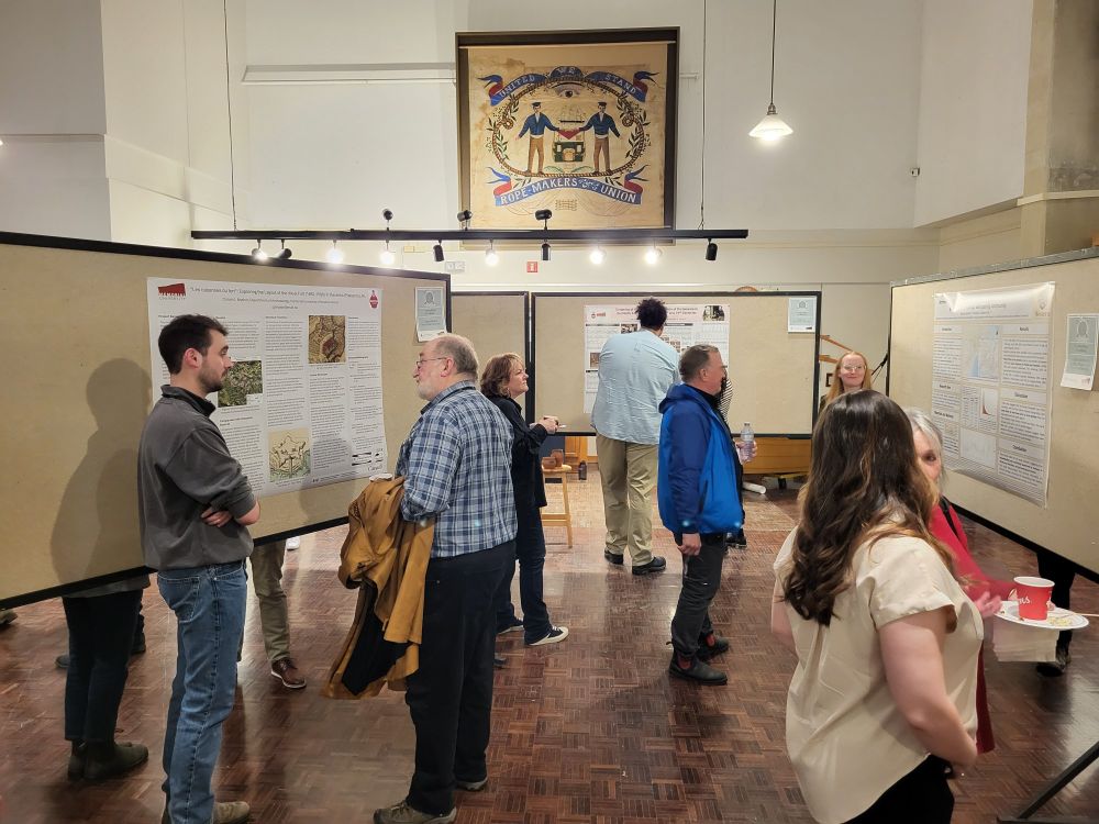 A group of people standing around in a large room, filled with rolling display boards. The boards have research posters on them, and the room is lit with warm lighting. 
