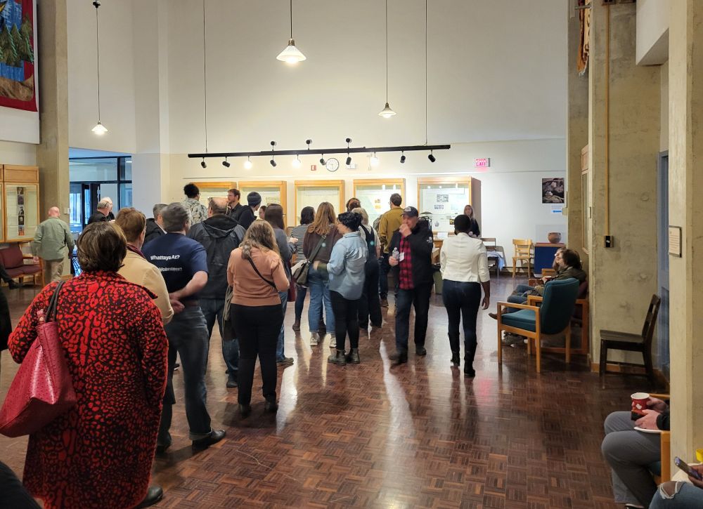A long line of people facing away from the camera, waiting for coffee on our morning coffee break. Everyone is standing in the great hall, a room with extremely high ceilings! 