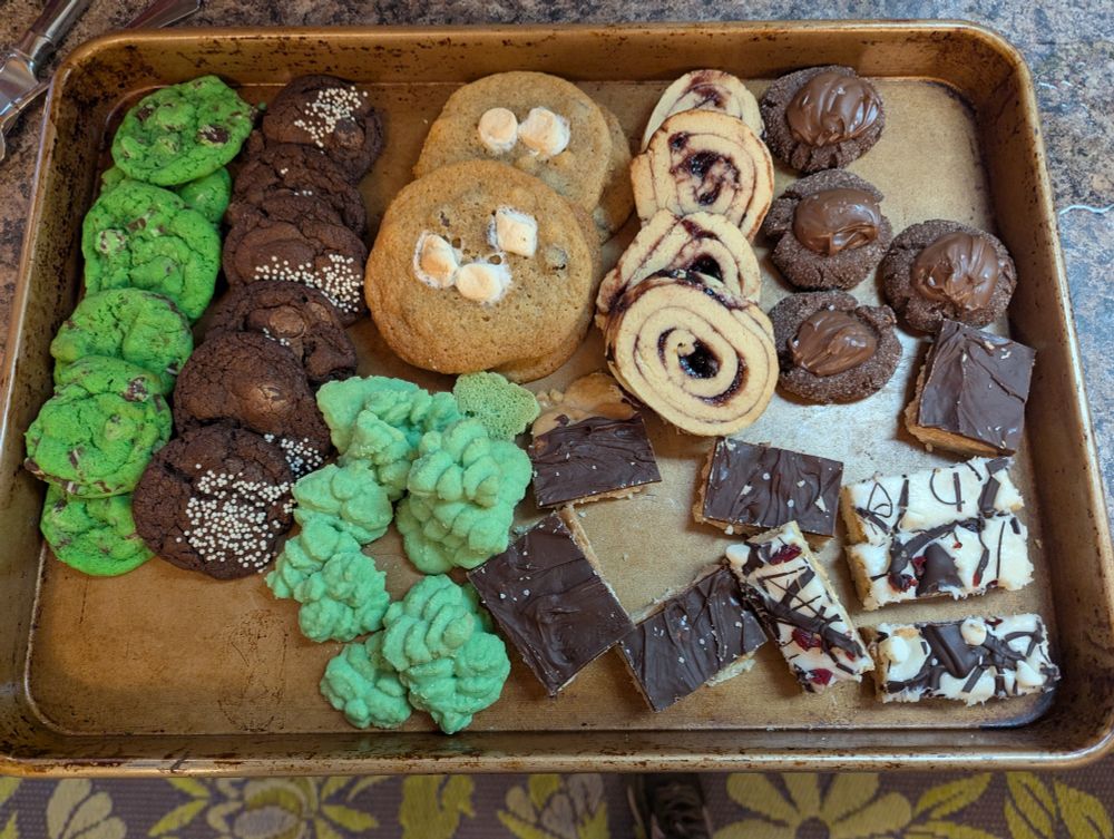 A tray of assorted cookies. Mint sugar cookies, midnight chocolate cookies, marshmallow white chocolate chip cookies, blackberry shortbread rollups, Nutella chocolate thumbprints, shortbread bars with toffee and chocolate, almond Christmas trees, and cranberry orange bars.