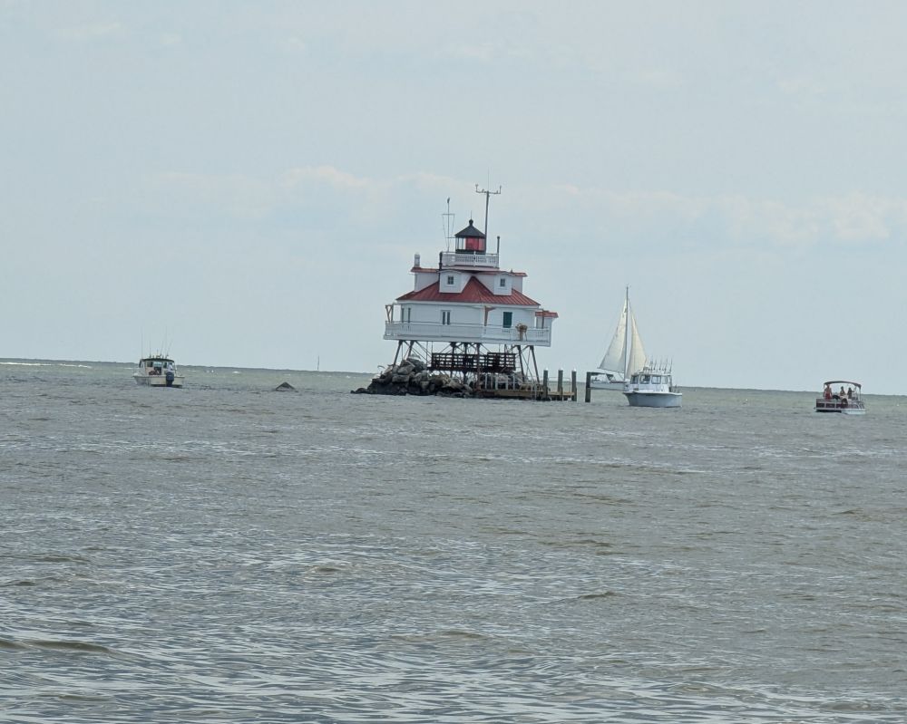 Thomas Point lighthouse, a short, octagonal wooden lighthouse built up on a platform over some rocks in the Chesapeake Bay. There are some small power boats anchored by the rocks, and the occupants were swimming and fishing.