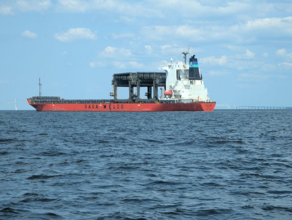 A huge cargo ship in the Chesapeake Bay. It was anchored outside the Bay Bridge, presumably waiting for its berth in the Port of Baltimore to become available. The ship has a long, red hull with "Saga Welcome" painted on the side. There is a white tower structure at the aft of the ship, and a black cargo loading/unloading structure (I think that's what it is) in front of that.
