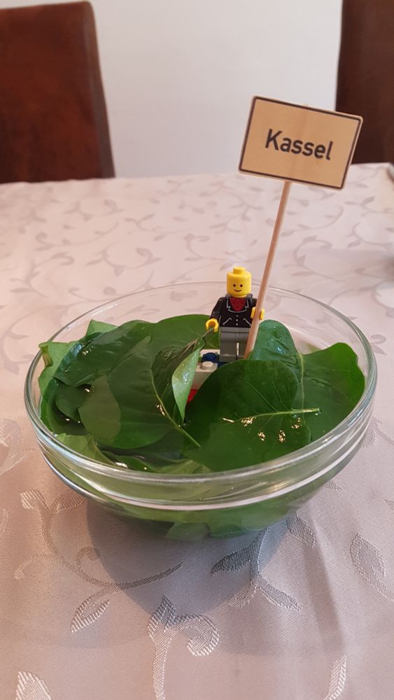 Legomännchen steht mit Ortsschild von Kassel in der Hand in einer Schale mit Blättern - Kasseler im Blätterteich