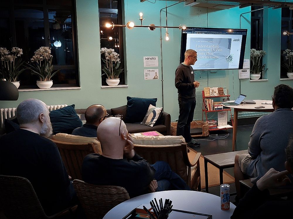 Jonny Allbut gives a presentation at the Bristol WordPress Meetup, speaking to an attentive audience in a cosy, modern room. The slide on screen reads “Understanding Common UX Pain Points That Frustrate Users.”